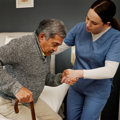 Female aide helping senior man get out of bed